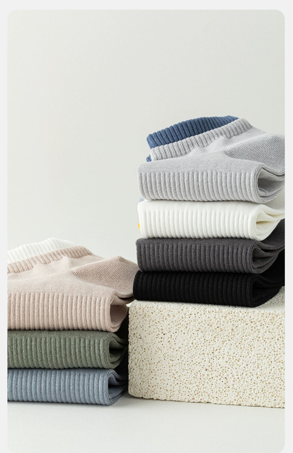 Stack of folded men's ribbed knit t-shirts in assorted colors on a textured block