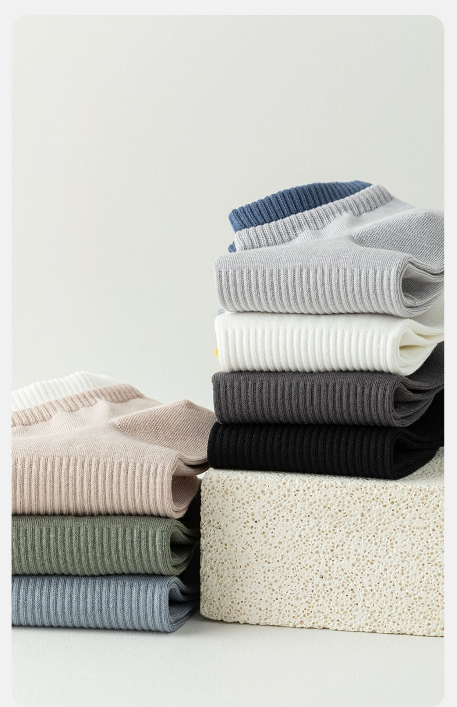 Stack of folded men's ribbed knit t-shirts in assorted colors on a textured block