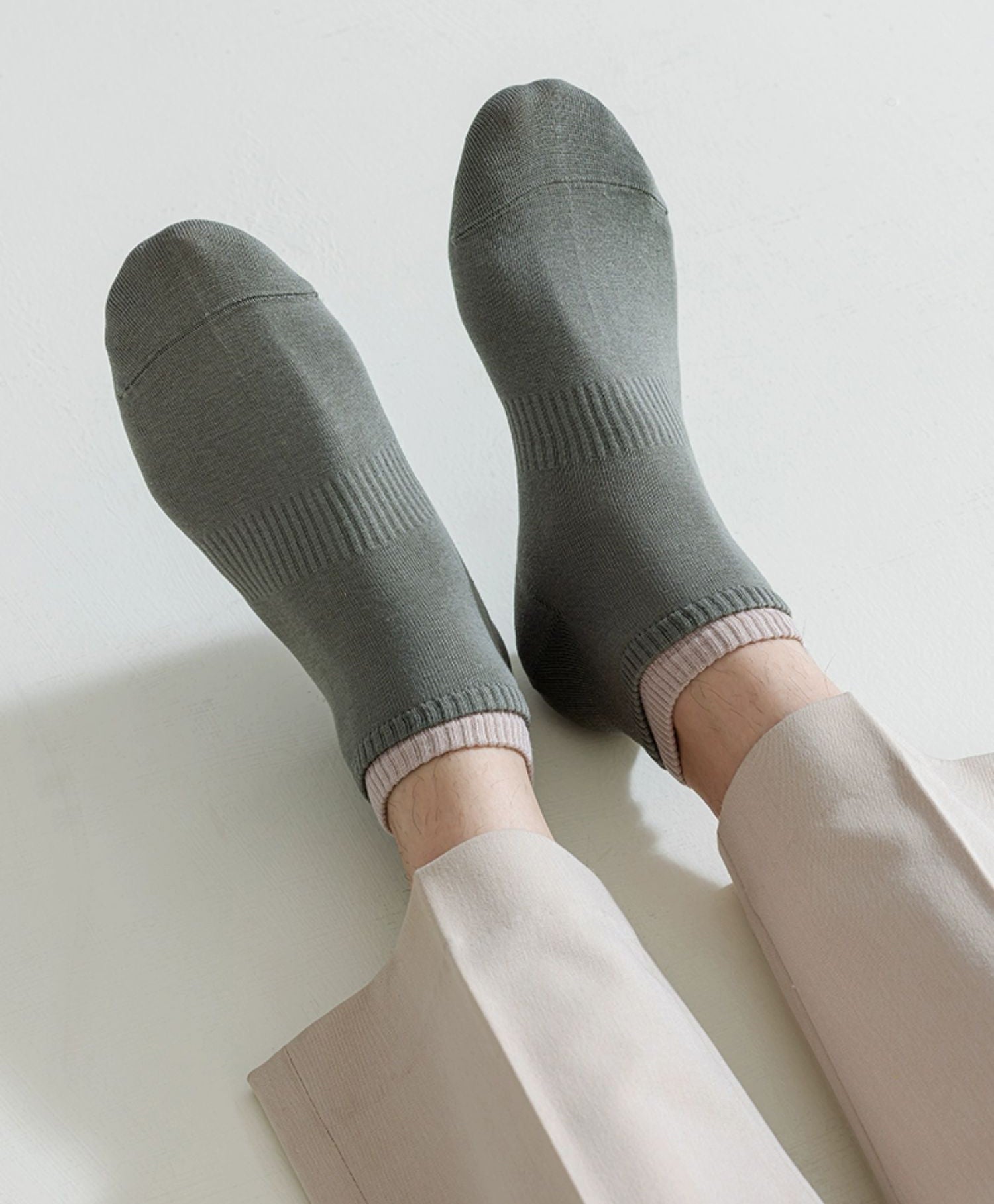Close-up of feet wearing olive green ankle socks with beige pants on a white background